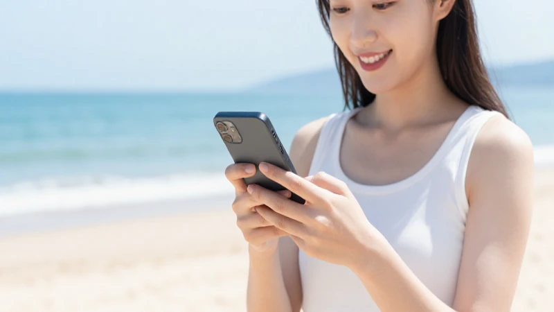 Mujer sonríe usando su móvil en la playa